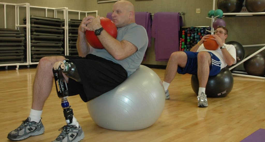 Un homme amputé de la jambe fait des exercises sur ballon. 