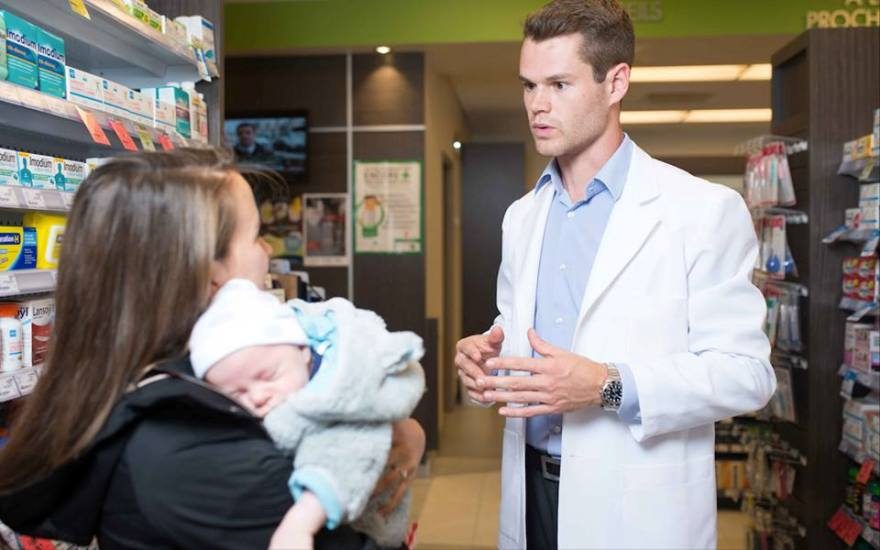 Un pharmacien répond à la question d'une femme qui tient un bébé. 