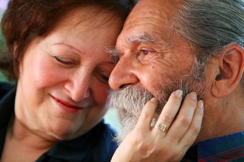 Gros plan d'un couple, la femme, qui semble un peu plus jeune, a les yeux fermés et a posé sa main sur la barbe grise d'un homme assez ridé.