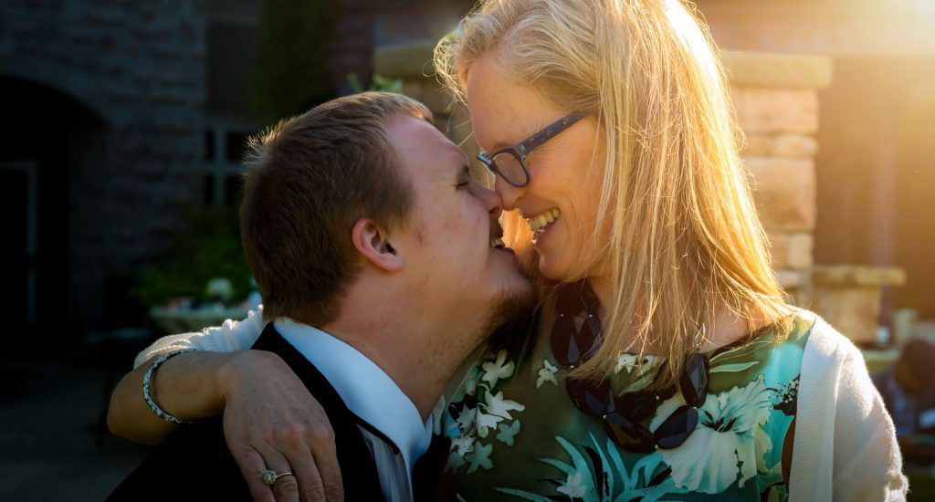 Un jeune garçon trisomique et sa mère, blonde avec des lunettes, se regardent dans les yeux.