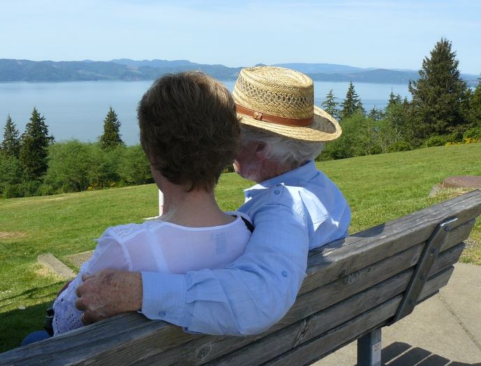 Un homme et une femme (aînés) regardent le fleuve, sur un banc de parc .