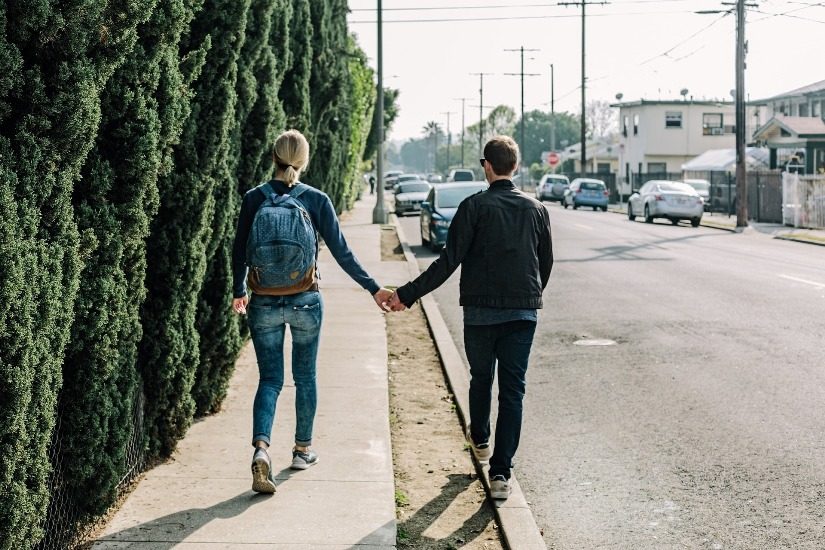 Une jeune femme et un jeune homme marchent sur le trottoir en se tenant la main. 