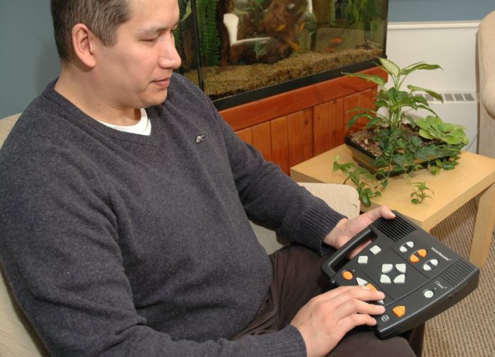 Un homme au cheveux bruns portant un chandail gris écoute un livre à l'aide d'un lecteur Victor.