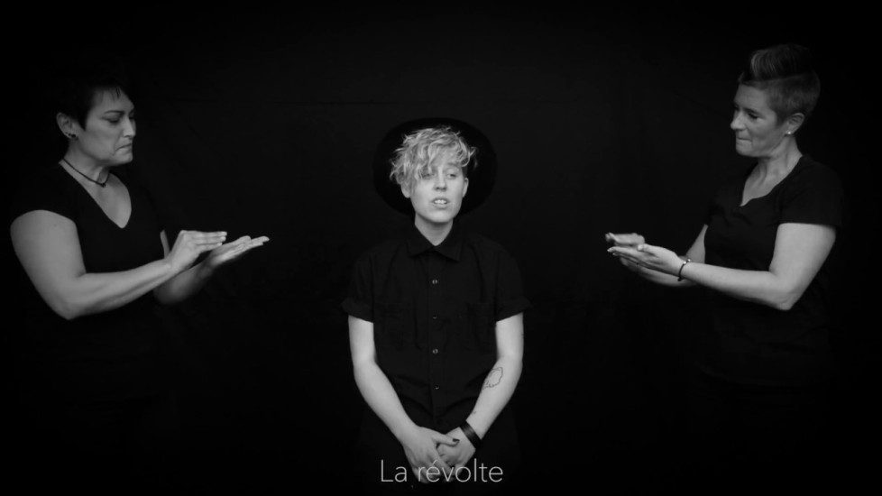 Photo en noir et blanc de la chanteuse Samuele, avec de chaque côté d'elle une interprète de la langue des signe du Québec.