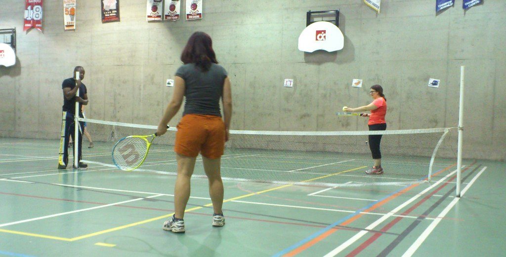Deux personnes jouent au tennis à l'intérieur d'un gymnase.

