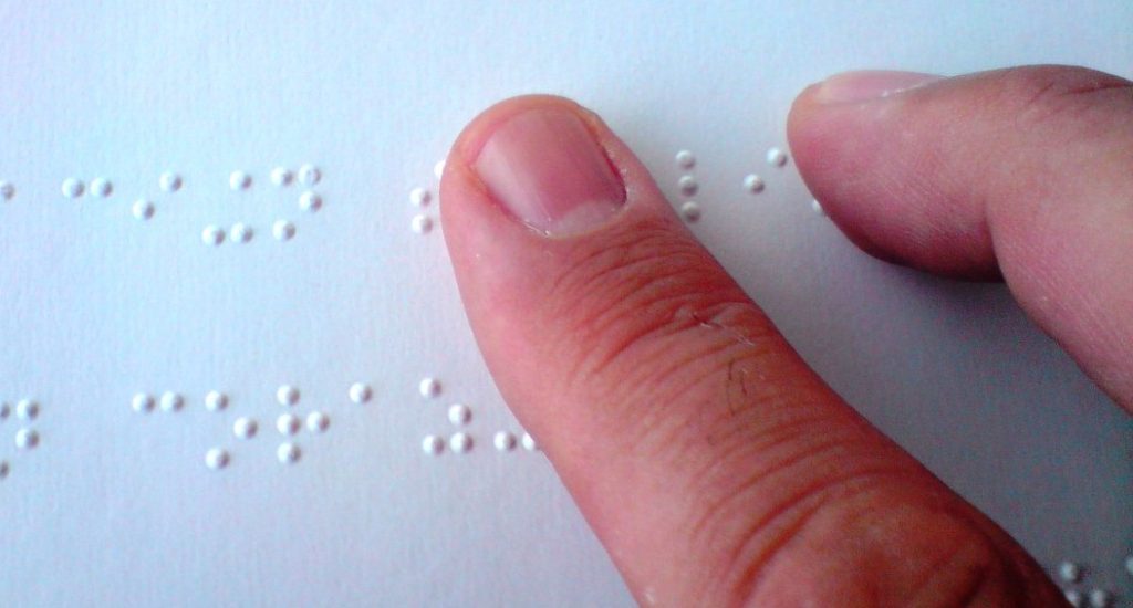 La photo montre un index qui glisse sur des caractères de braille.