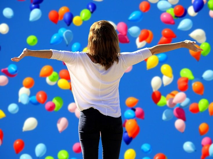 On voir une femme de dos et pleins de ballons multicolores sur un ciel très bleu.