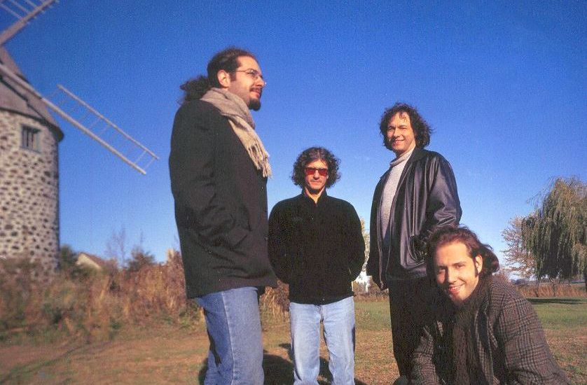 Le groupe Le Vent du Nord en 2003. Ils posent près d'un moulin de pierre devant un ciel très bleu. De gauche à droite: Nicolas Boulerice,, Bernard Simard, Benoit Bourque, Olivier Demers.