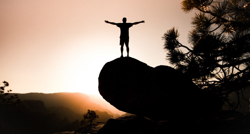 Un homme debout sur un rocher au levé du soleil.