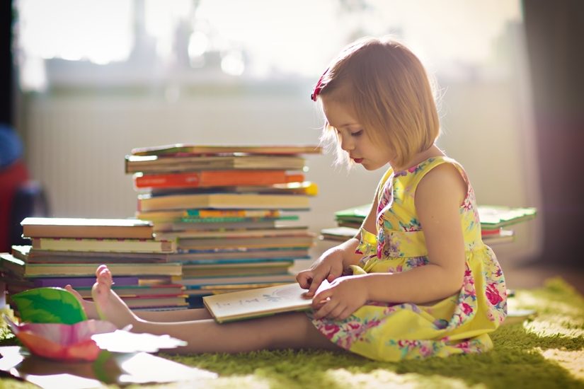 une fillette qui porte une robe jaune lit un livre. Elle est assise par terre à côté d'une pile de livres. une fillette qui porte une robe jaune lit un livre. Elle est assise par terre à côté d'une pile de livres.