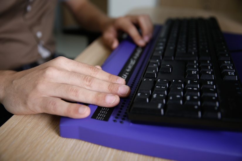 Deux mains d'hommes sur un clavier d'ordinateur qui comprend un module pour le braille.