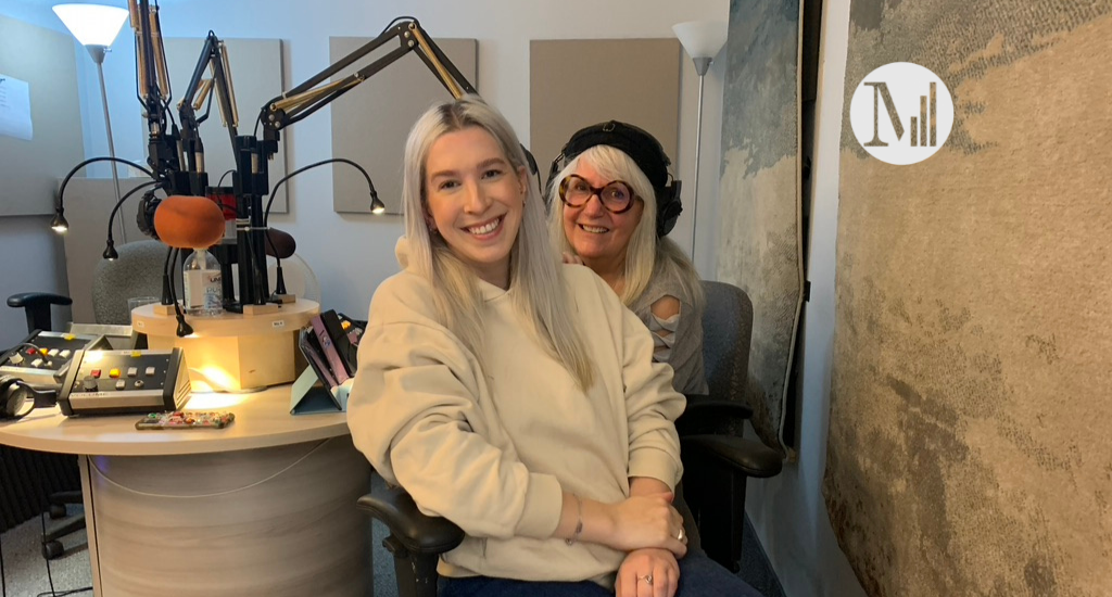 Arlette et son invitée Marianne Plaisance dans les studios de Canal M. Marianne Plaisance est assise au premier plan et porte un coton ouaté beige. Elle a les cheveux teinté presque de la même couleur que son coton ouaté. Elle a aussi les cheveux de la même couleur qu'Arlette