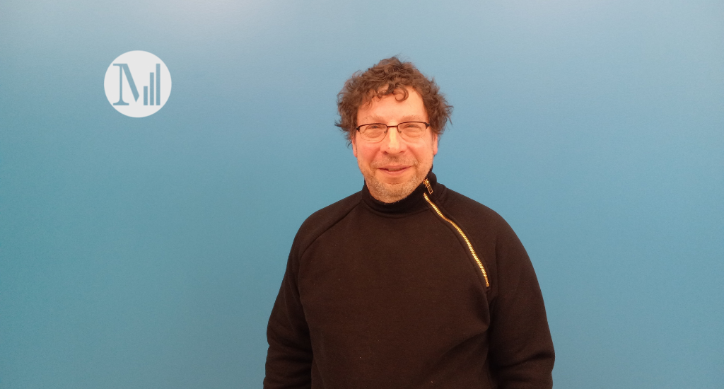 L'animateur Yvan Deslauriers, un homme brun aux cheveux bouclés portant des lunettes devant le mur bleu de Canal M