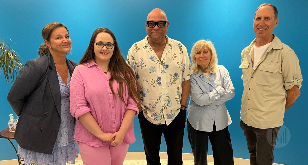 Chantal LAvoie, Nathalie Barette et leur invités posent devant un mur bleu.