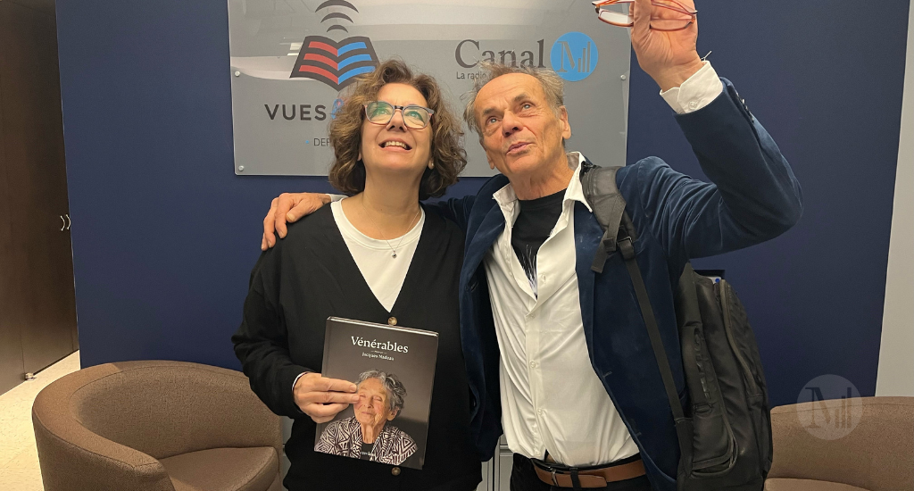 Hélène Denis et Jacques Nadeau posent à l'entrée de Canal M avec l'album photo «Vénérables» en regardant vers le haut.