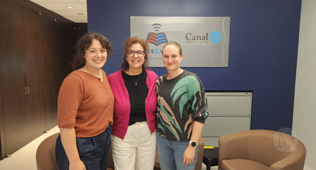 Rose-Anne Déry, Hélène Denis et Kim Despatis prennent la pose devant le panneau publicitaire de Vues&Voix/Canal M. 
